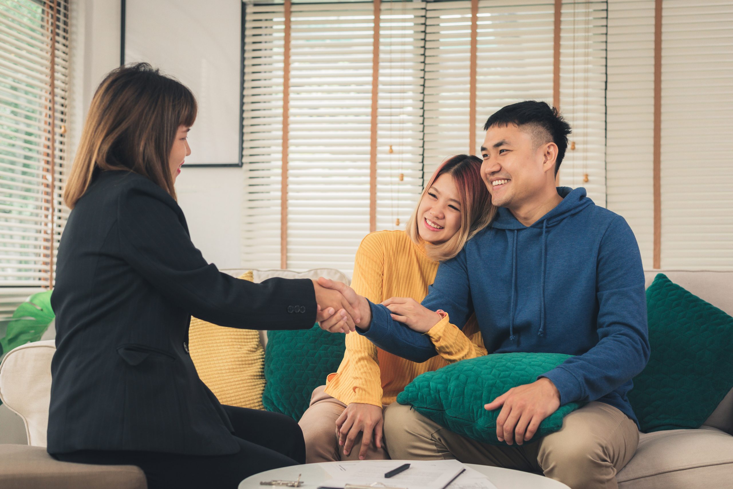 Happy young couple meeting with an Asset Protection attorney, shaking hands in a warm and welcoming office environment, discussing strategies to safeguard their family's wealth.