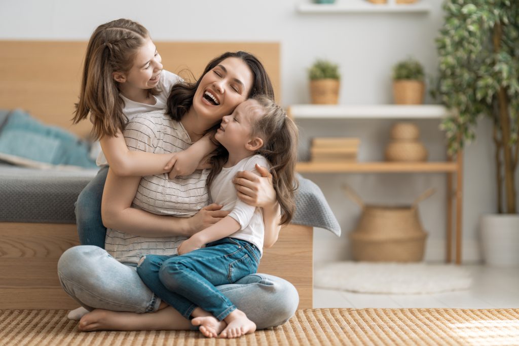 A happy mother sitting on the floor with her two daughters, laughing and embracing each other. Perfect family moment highlighting the importance of family relationships. Best Family Law Attorney in Illinois can help protect and guide your family through legal matters.