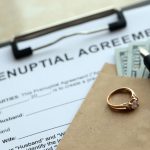 Prenuptial agreement and wedding ring on table. Premarital paperwork process in USA close up