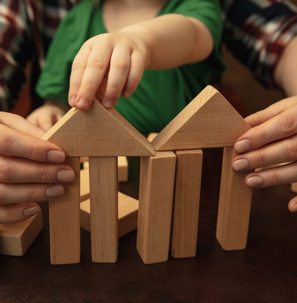 A child and an adult assembling a house structure with wooden blocks, symbolizing family security and stability, related to services provided by an Asset Protection Attorney in Park Gold Group.